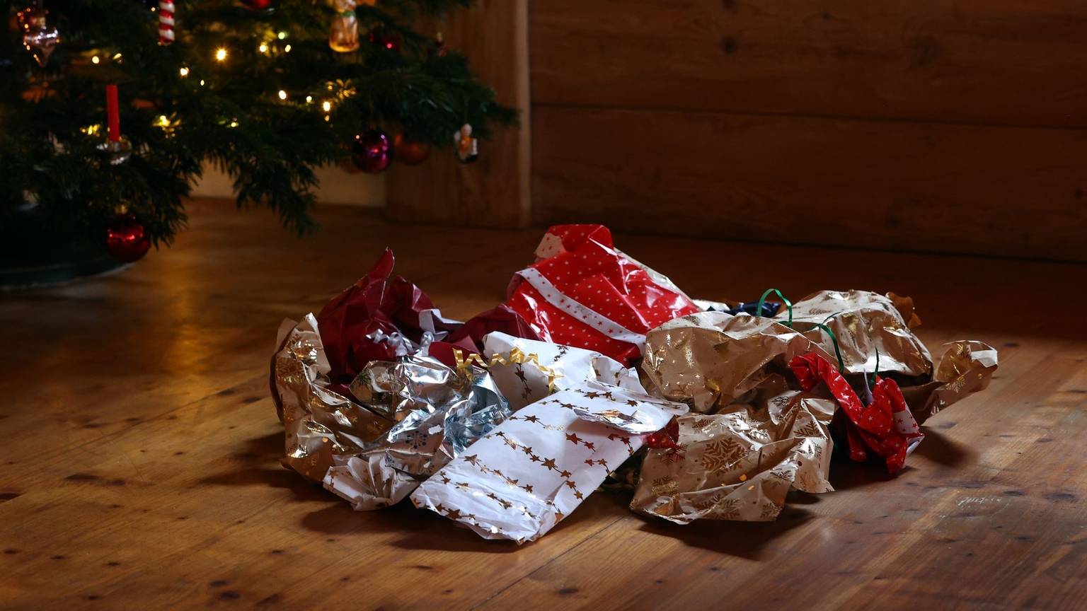 Zerknülltes Geschenkpapier auf einem Holzboden unter einem Weihnachtbaum.