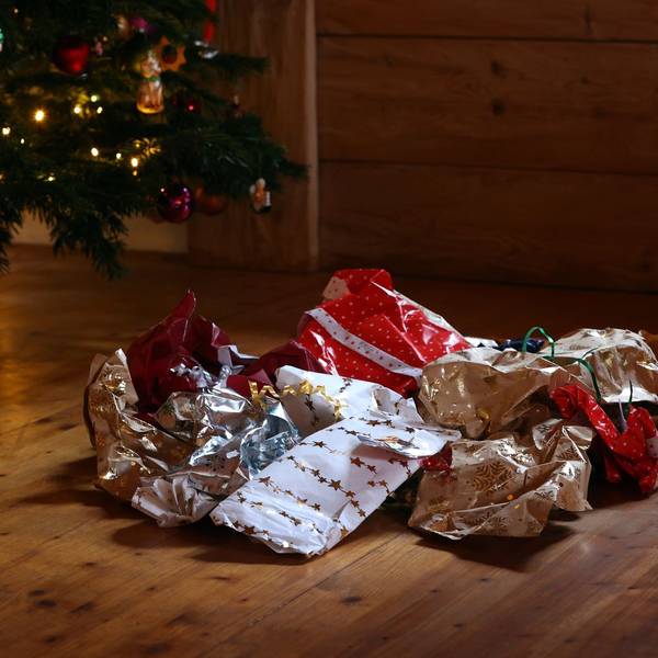 Zerknülltes Geschenkpapier auf einem Holzboden unter einem Weihnachtbaum.