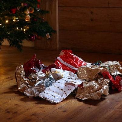 Zerknülltes Geschenkpapier auf einem Holzboden unter einem Weihnachtbaum.