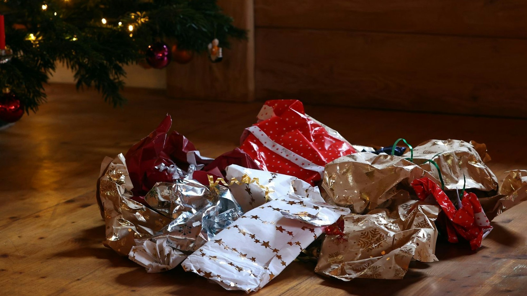 Zerknülltes Geschenkpapier auf einem Holzboden unter einem Weihnachtbaum.