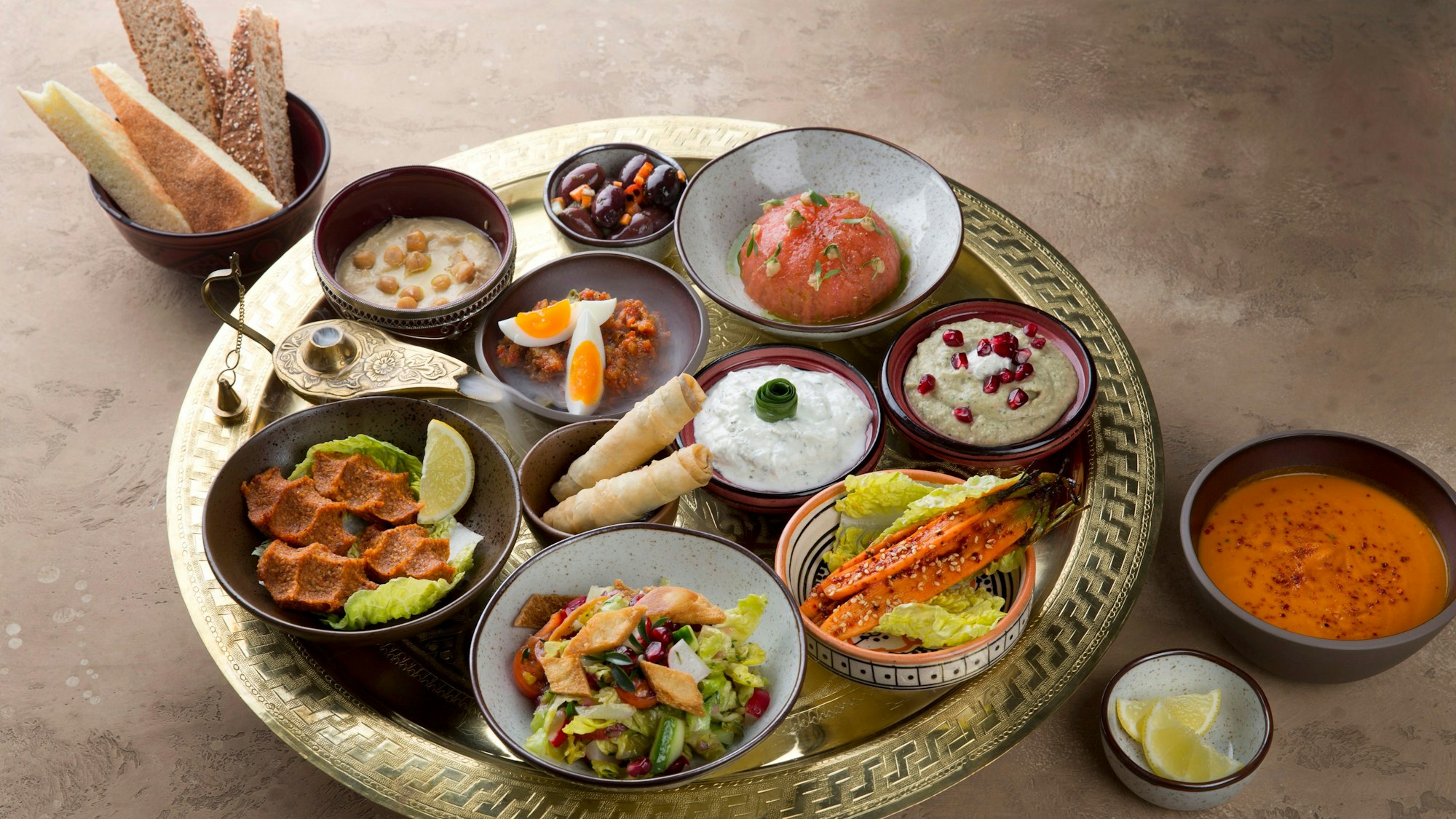 Mezze-Platte, angerichtete Speisen in kleinen Schälchen auf einem Tablett mit Brot.