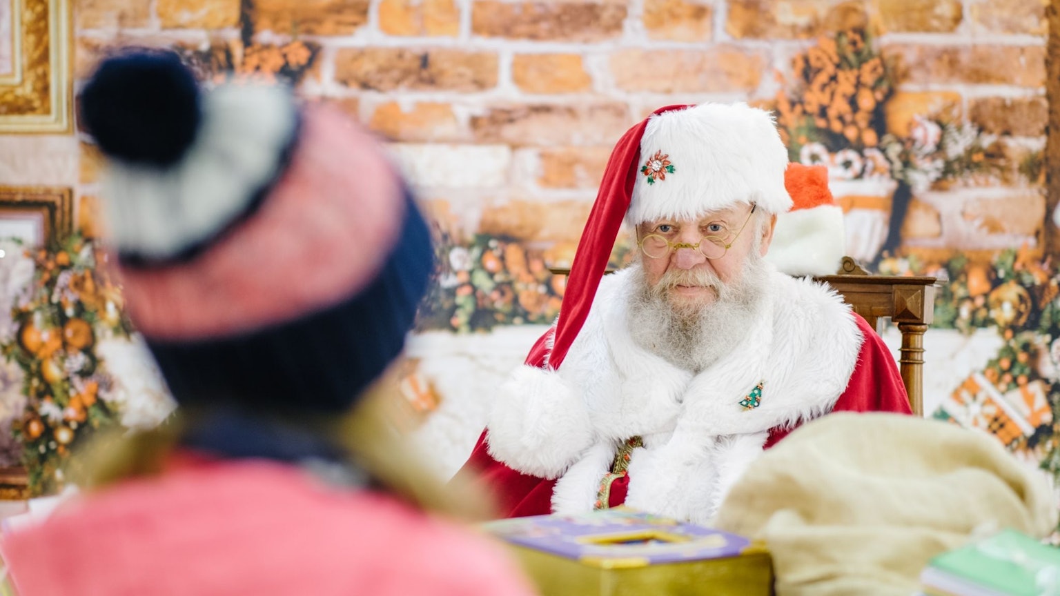 Ein Mann im Weihnachtsmann-Kostüm blickt einem Mädchen ins Gesicht.
