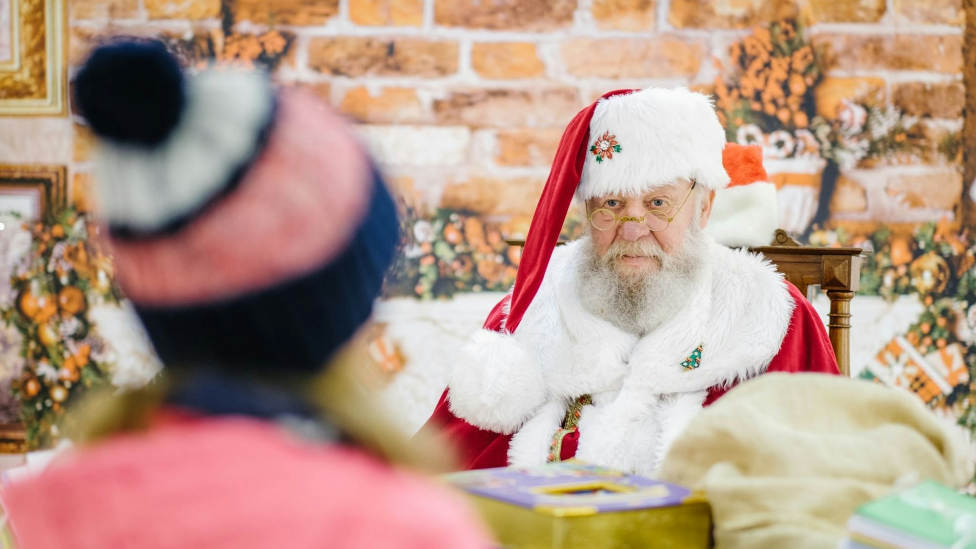 Ein Mann im Weihnachtsmann-Kostüm blickt einem Mädchen ins Gesicht.