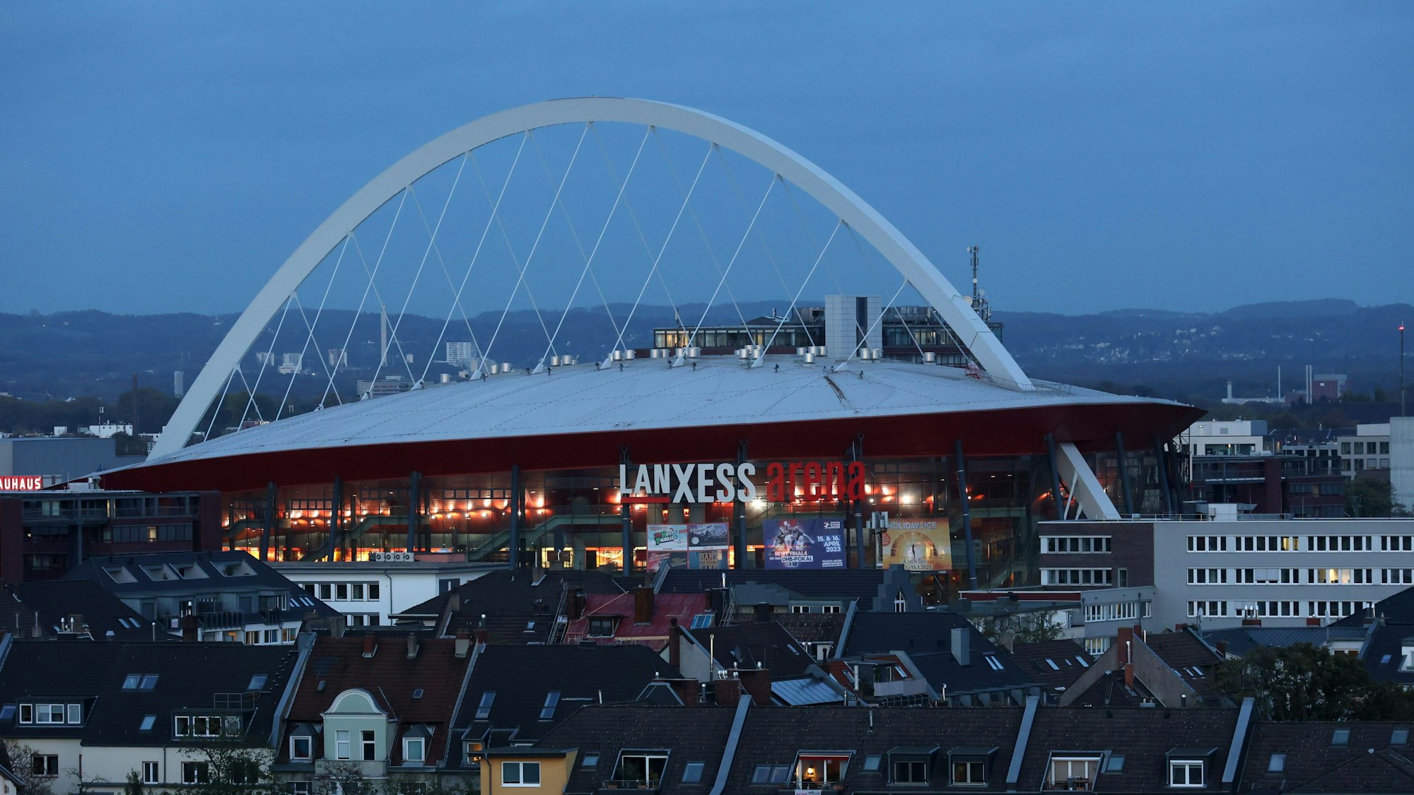 Die Lanxess-Arena von einem erhöhten Standpunkt gesehen, im Vordergrund Häuser.