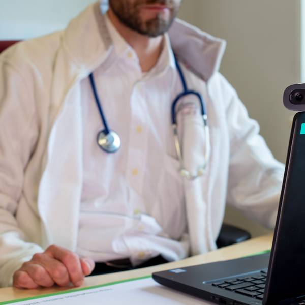 Ein Hausarzt spricht während einer Videosprechstunde in seiner Praxis mit einer Patientin.