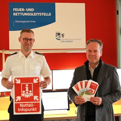 Leitstellen-Chef Julian Seeger (l.) und Kreisdirektor Klaus Grootens halten ein knallrote Symbol in der Hand, das bei einem Stromausfall auf Notfallpunkte hinweisen soll.