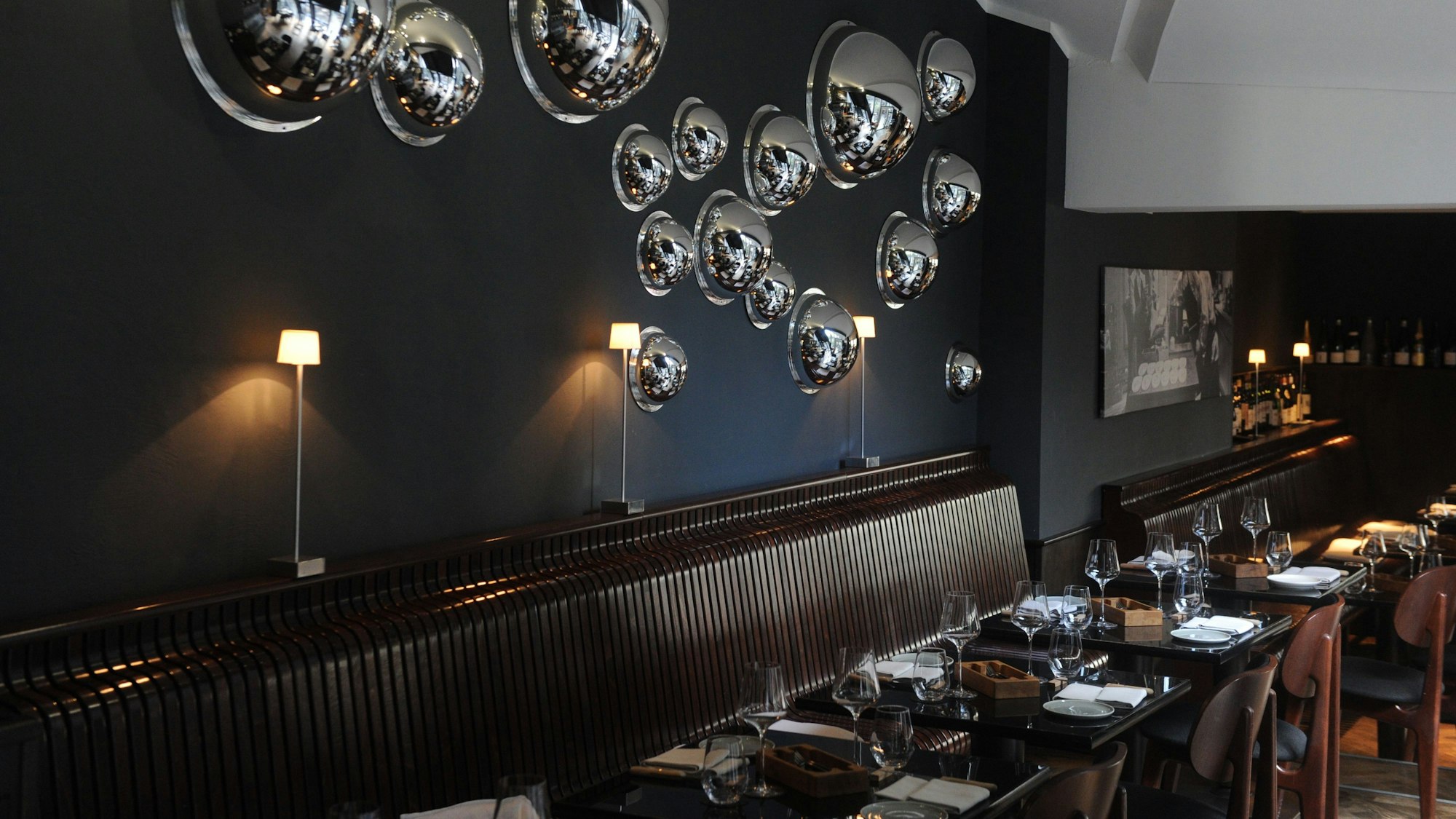 Bank und gedeckte Tische vor einer dunklen Wand mit runden Spiegelinstallationen.