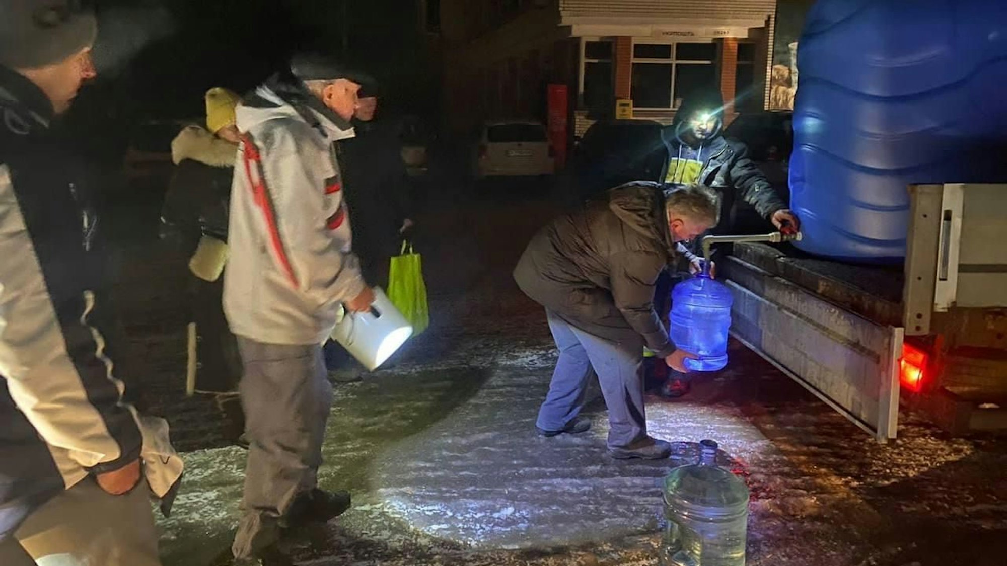 Menschen mit Eimern füllen Wasser an einem großen Tank von der Ladefläche eines Kleinlasters ab.
