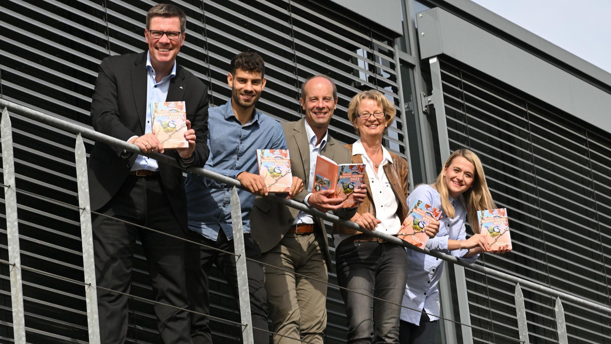 Landrat Stephan Santelmann, Claudio Heider, Hans-Martin Heider, Karin Grunewald und Charlotte Loesch stehen nebeneinander mit einem Kalender-Exemplar auf einer Empore.