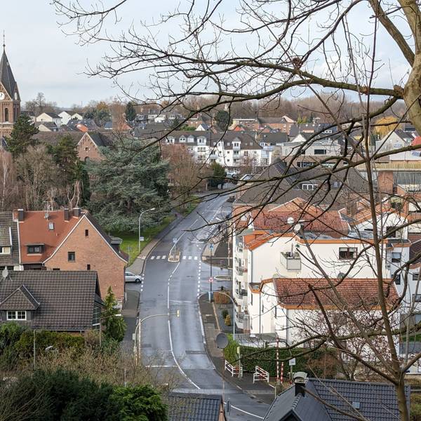 Ansicht von Alt-Hürth mit Straße und Kirche, bewölkt.