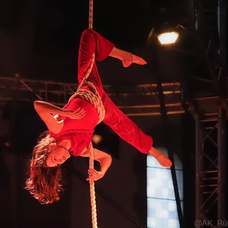 Die 39-Jährige hängt kopfüber an einem Seil, das um ihre Hüfte gewickelt ist, in der Kirche. Sie trägt rote Kleidung und offene Haare.