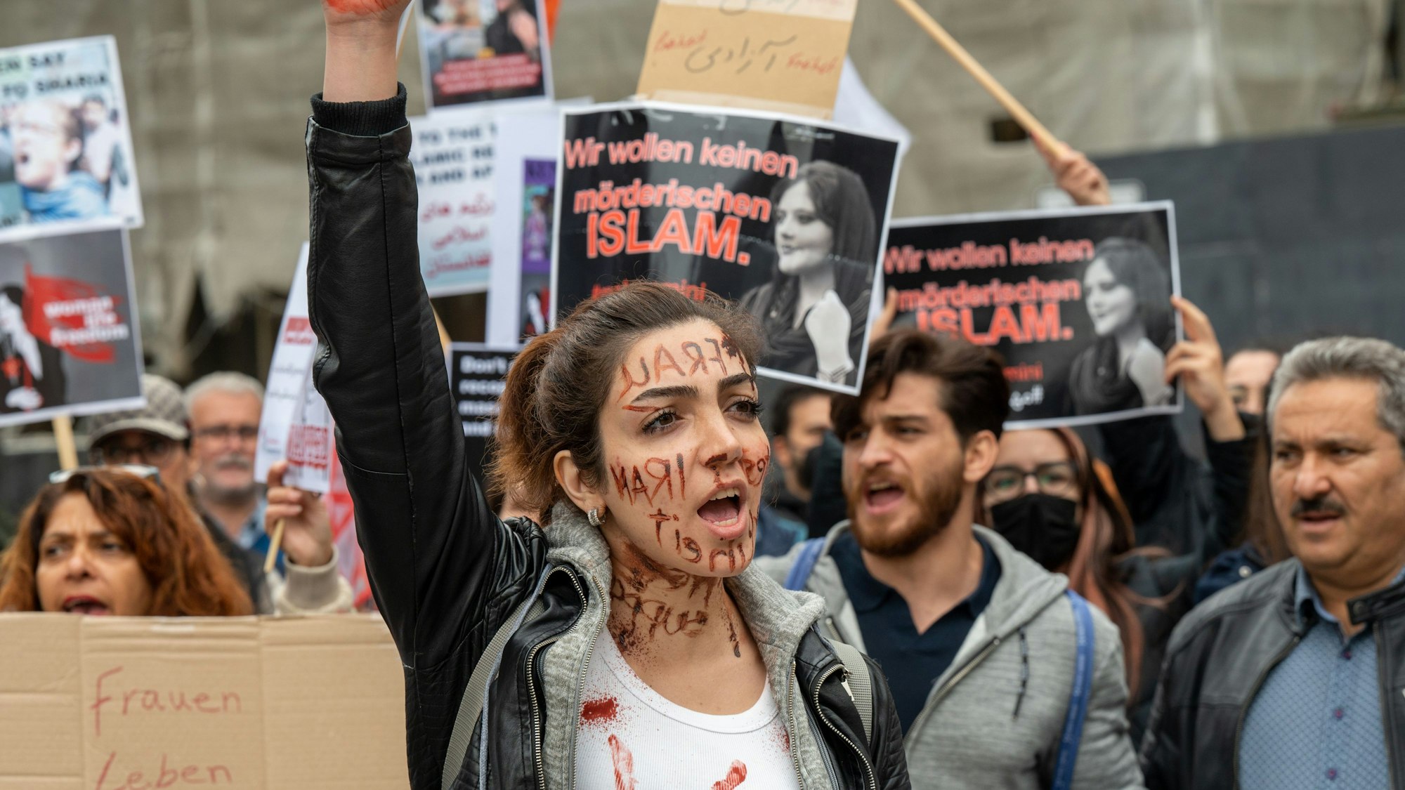 Eine Frau demonstriert in der Kölner Innenstadt. Im Hintergrund halten mehrere Menschen Schilder in die Luft.