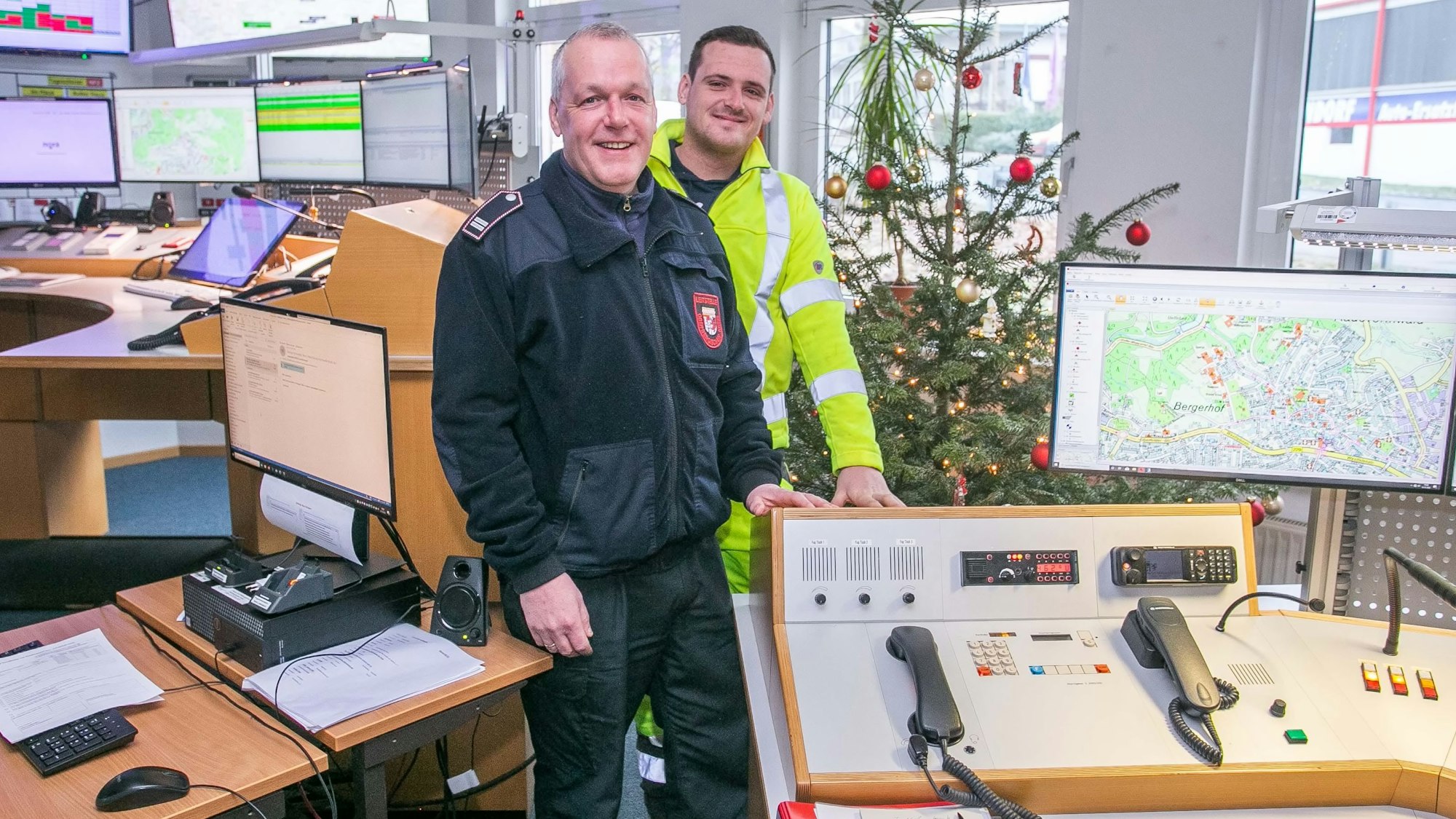 Ralf Breloer steht mit seinem Sohn Patrick in der Wache. Mehrere Bildschirme und Telefone stehen im Vorder- und Hintergrund.