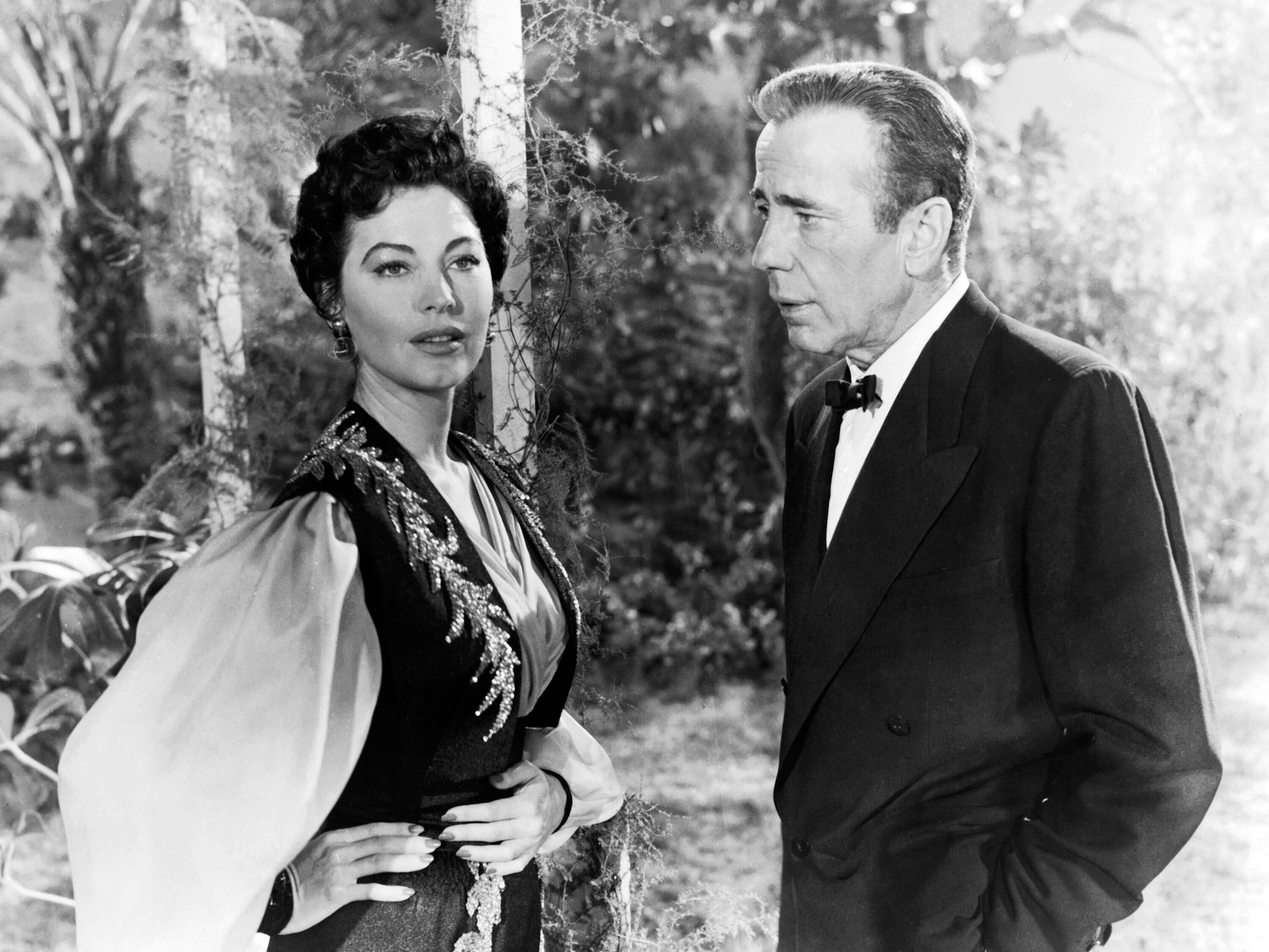 Ava Gardner und Humphrey Bogart stehen draußen und reden miteinander.