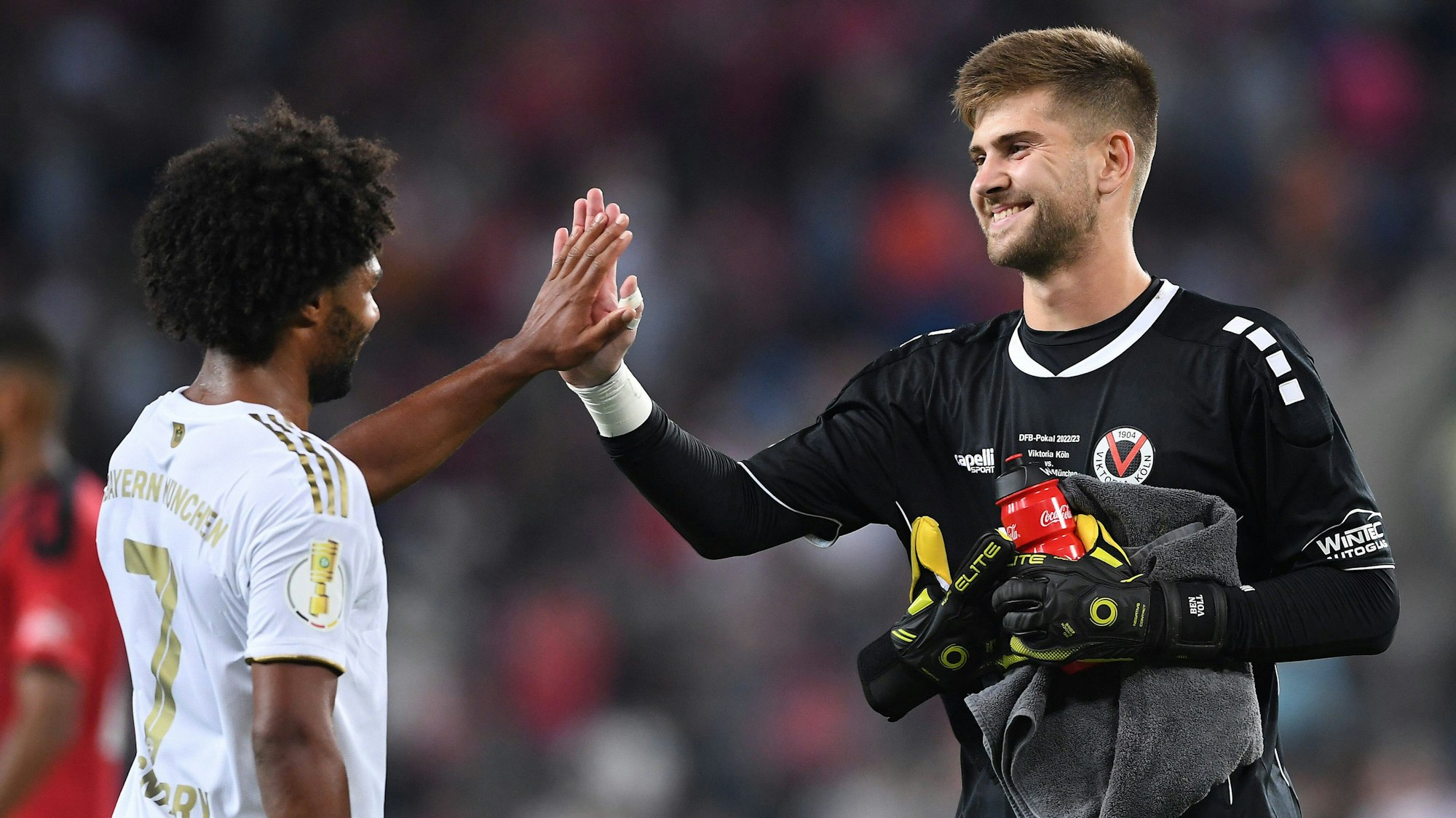 Zwei Fußballspieler geben sich nach einem Spiel die Hand und lächeln.