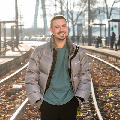 Sänger Sebastian Wurth, Ex-Mitglied der Schlager Boyband „Feuerherz“, will nun solo mit Popmusik auf Deutsch durchstarten. Er steht in Winterjacke an der Haltestelle Deutzer Freiheit.