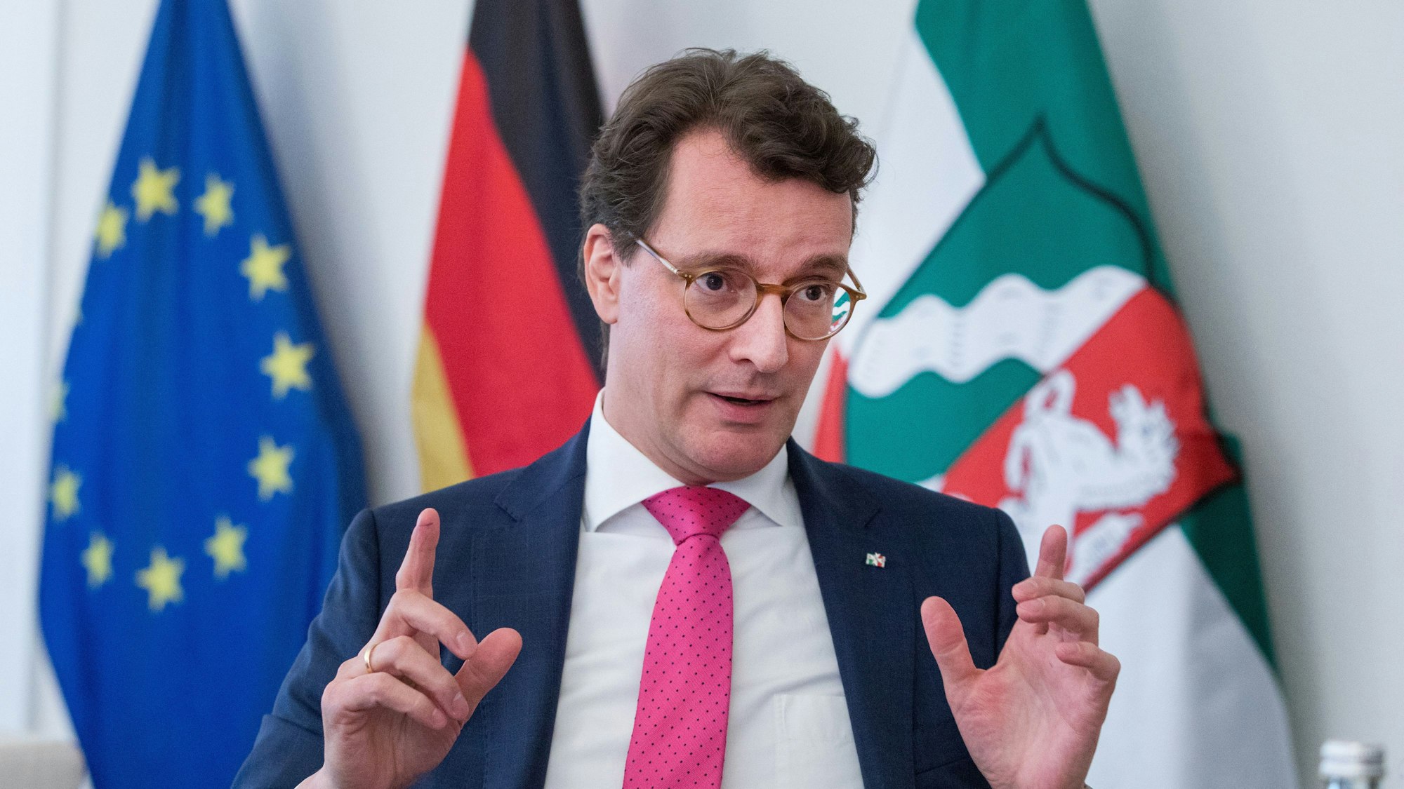 Hendrik Wüst, kurz vor Weihnachten im Gespräch mit dem „Kölner Stadt-Anzeiger“. Hinter ihm stehen drei Fahnen, die der EU, Deutschlands und von Nordrhein-Westfalen.