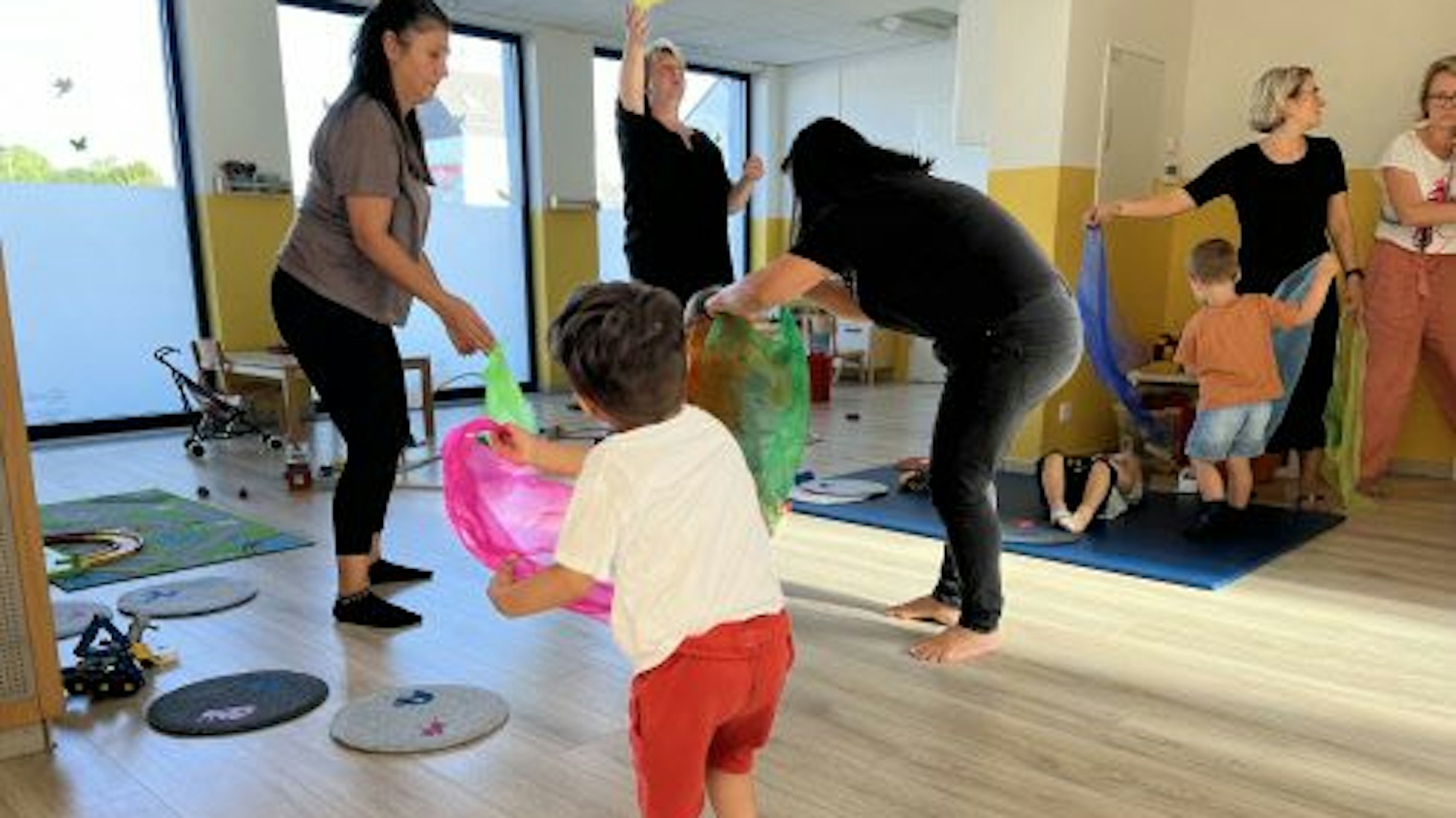 Mehrere Kinder und Erwachsene spielen in einem Raum mit Schwungtüchern.