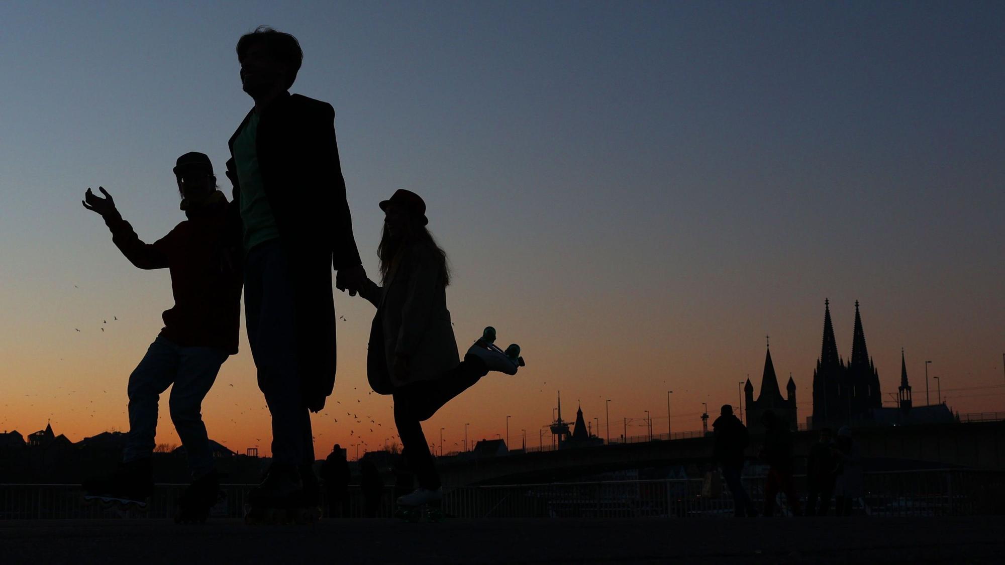 Im März tanzen drei Freunde auf Rollschuhen bei Dämmerung vor dem Stadtpanorama.