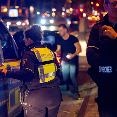 Ein Polizeiwagen steht auf einer Straße. Eine Polizistin steht an dem Wagen.