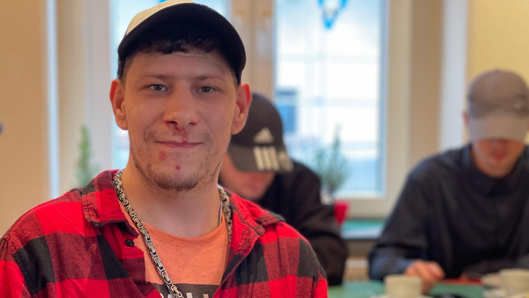 Kevin am Tisch, im Hintergrund zwei junge Männer