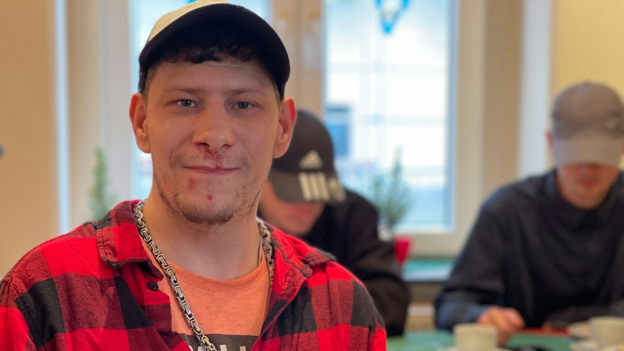 Kevin am Tisch, im Hintergrund zwei junge Männer