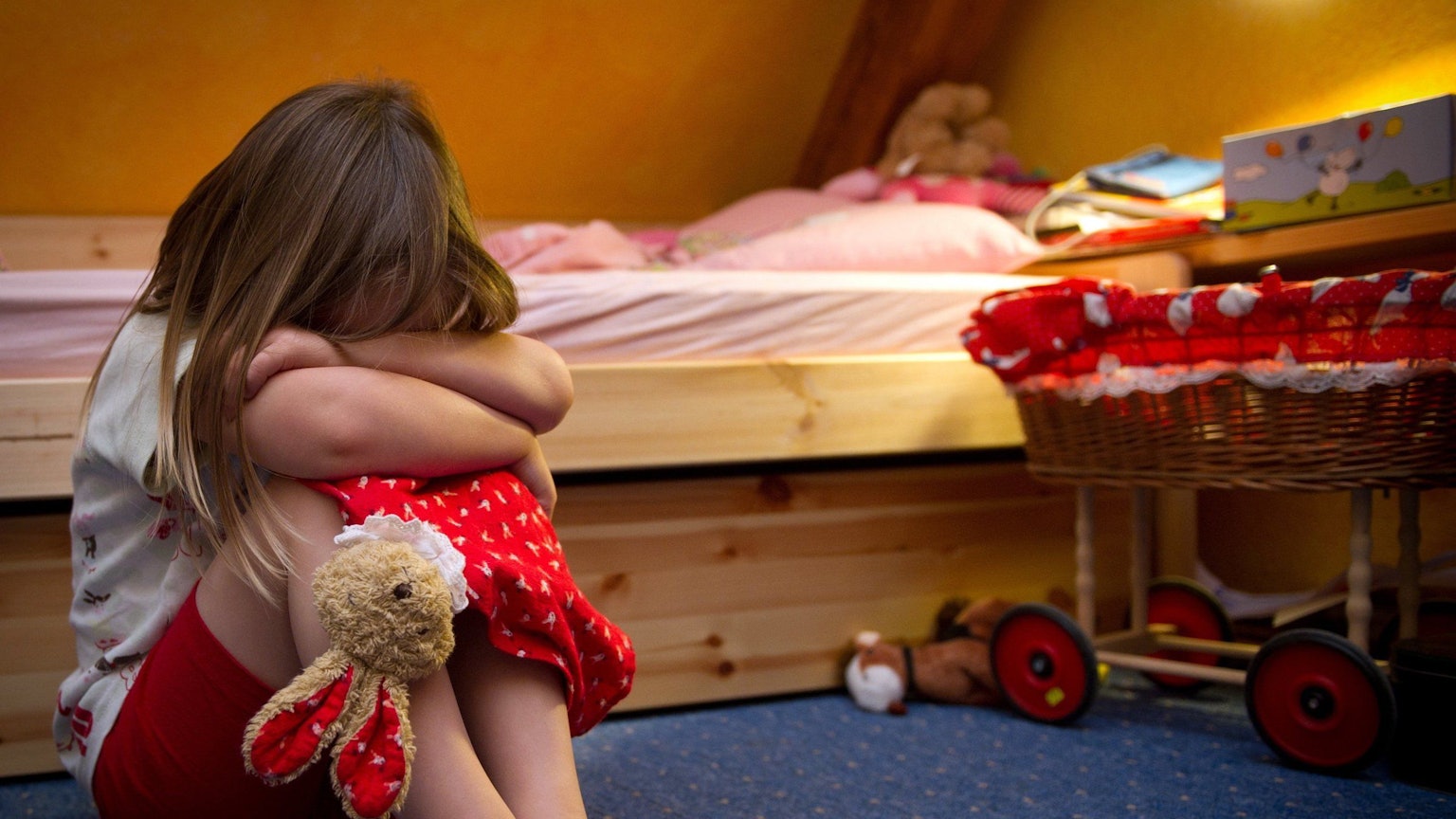 Ein kleines Mädchen sitzt weinend auf dem Fußboden in ihrem Zimmer.