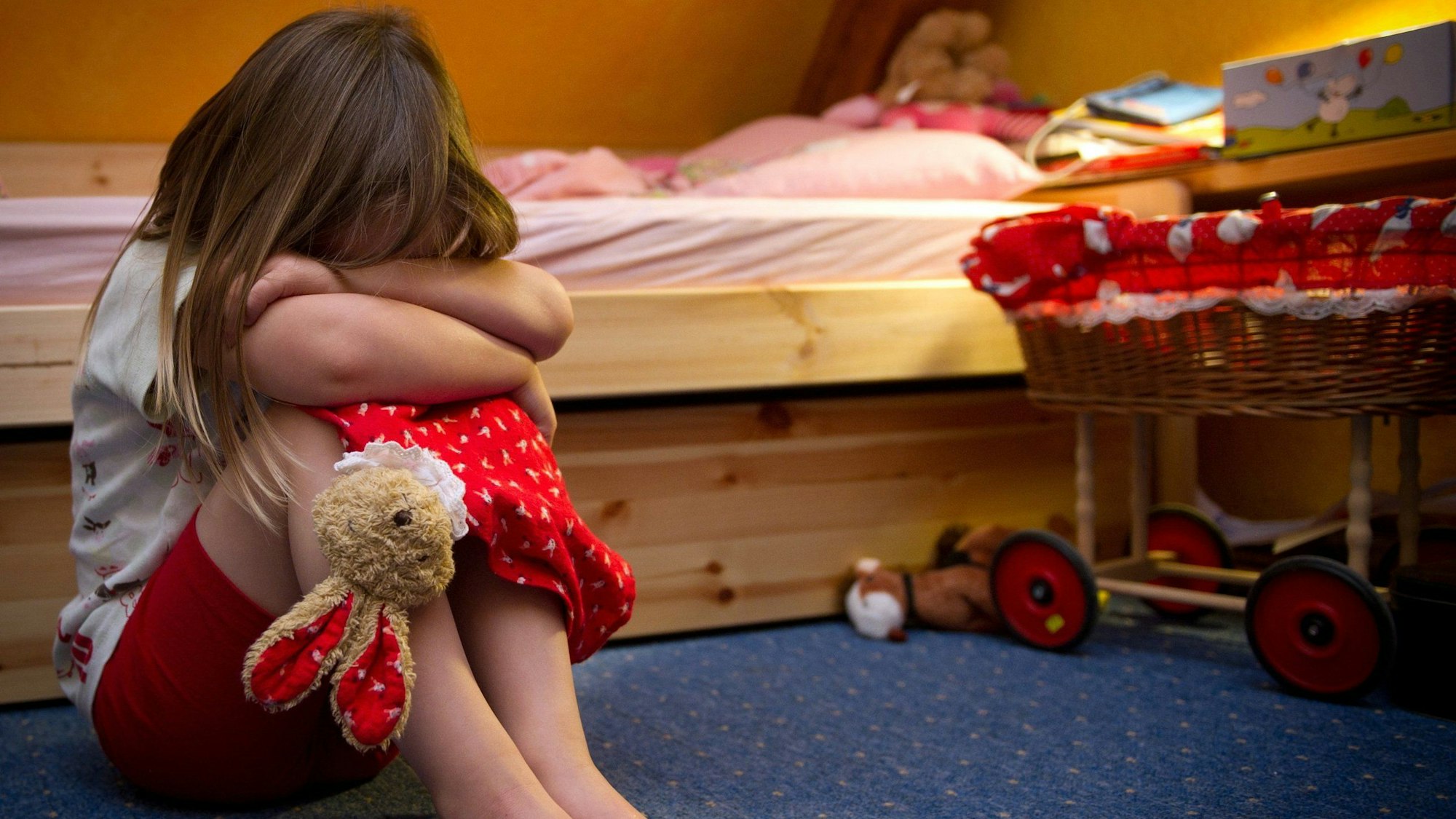 Ein kleines Mädchen sitzt weinend auf dem Fußboden in ihrem Zimmer.