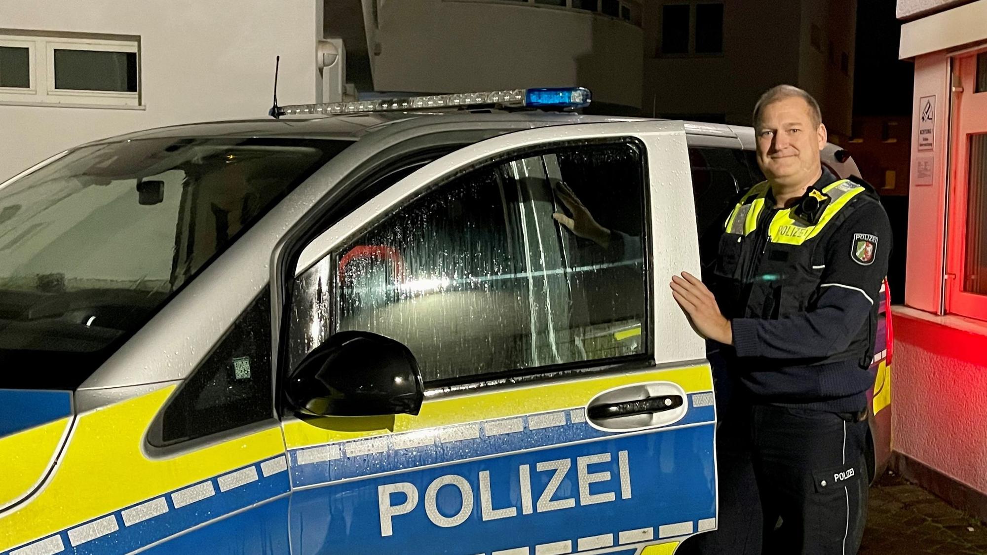 Ein Polizist in Uniform steht an der geöffneten Tür eines Streifenwagens. Es ist Nacht.