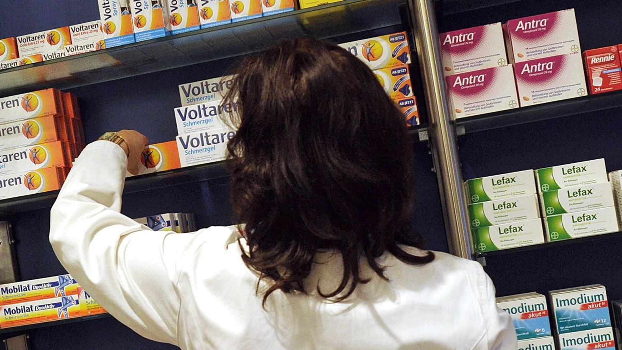 Eine Apothekerin nimmt ein Medikament aus dem Regal.