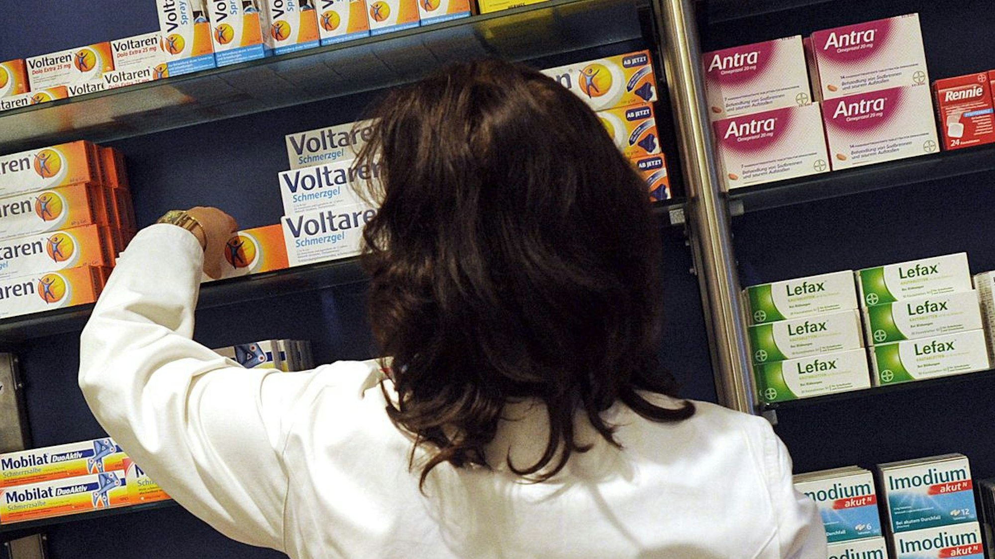 Eine Apothekerin nimmt ein Medikament aus dem Regal.