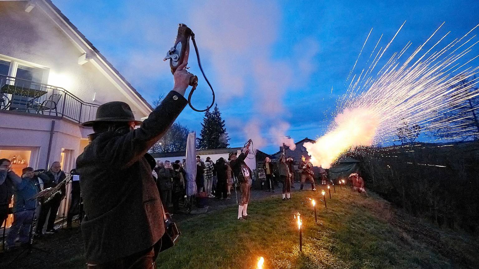 Das Foto zeigt den Moment, als sich die speziellen Böllerpistolen der in Trachten gekleideten Schützen mit Blitz, Rauch und mächtigem Getöse in den Abendhimmel entladen.