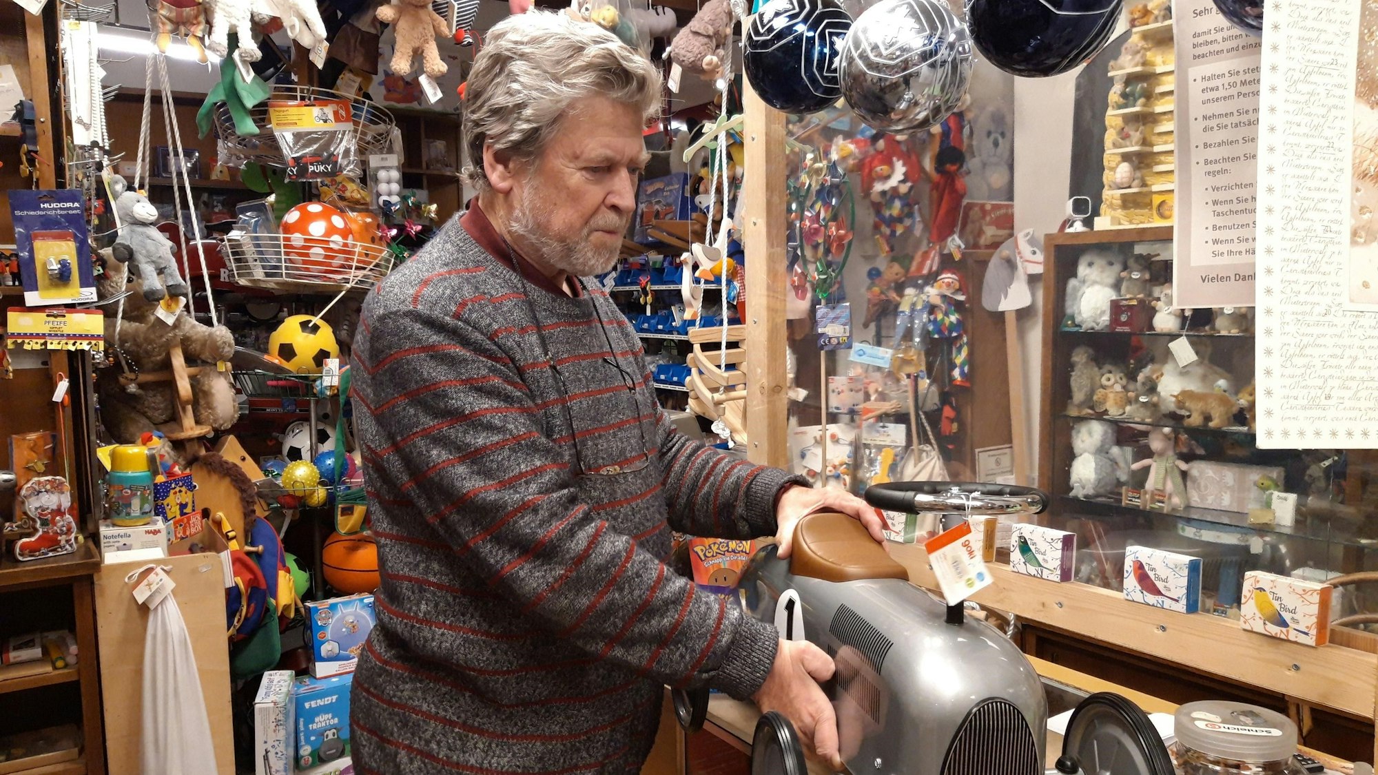 Inhaber Dieter van Dillen hält in seinem Laden ein silbernes Rutschauto in der Hand.