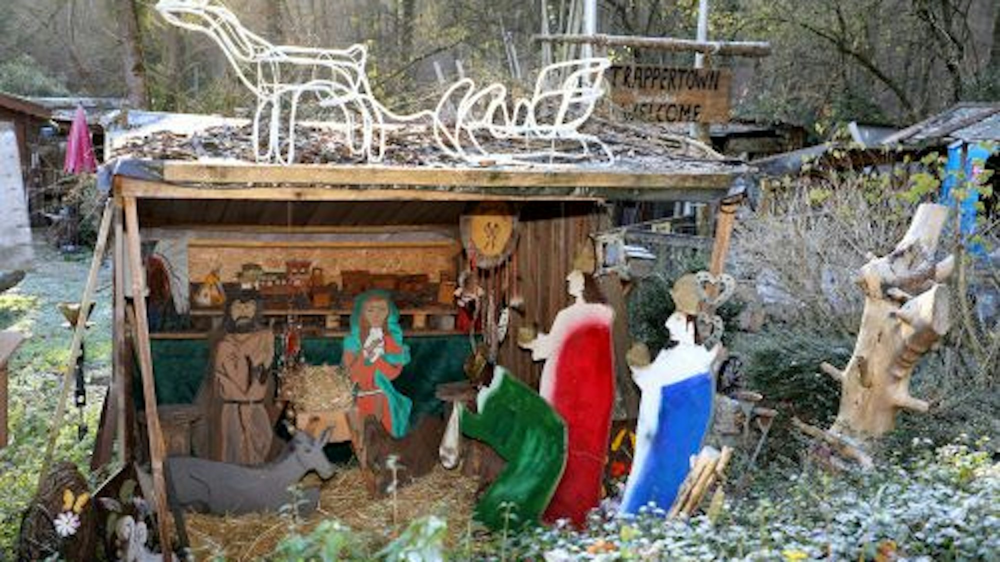 Bunte Krippenfiguren stehen in einem Garten.