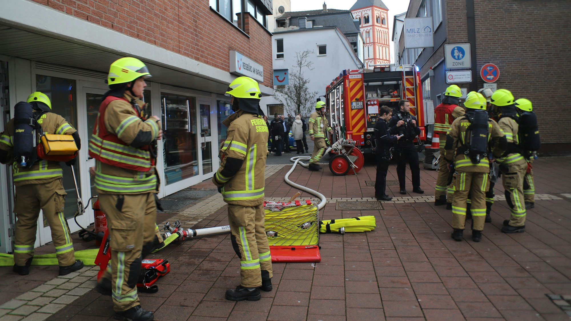 Feuerwehrleute stehen auf dem gepflasterten Nogener Platz neben dem gläsernen Eingang. Ein dicker Schlauch liegt auf dem Boden bis zum Feuerwehrauto im Hintergrund.