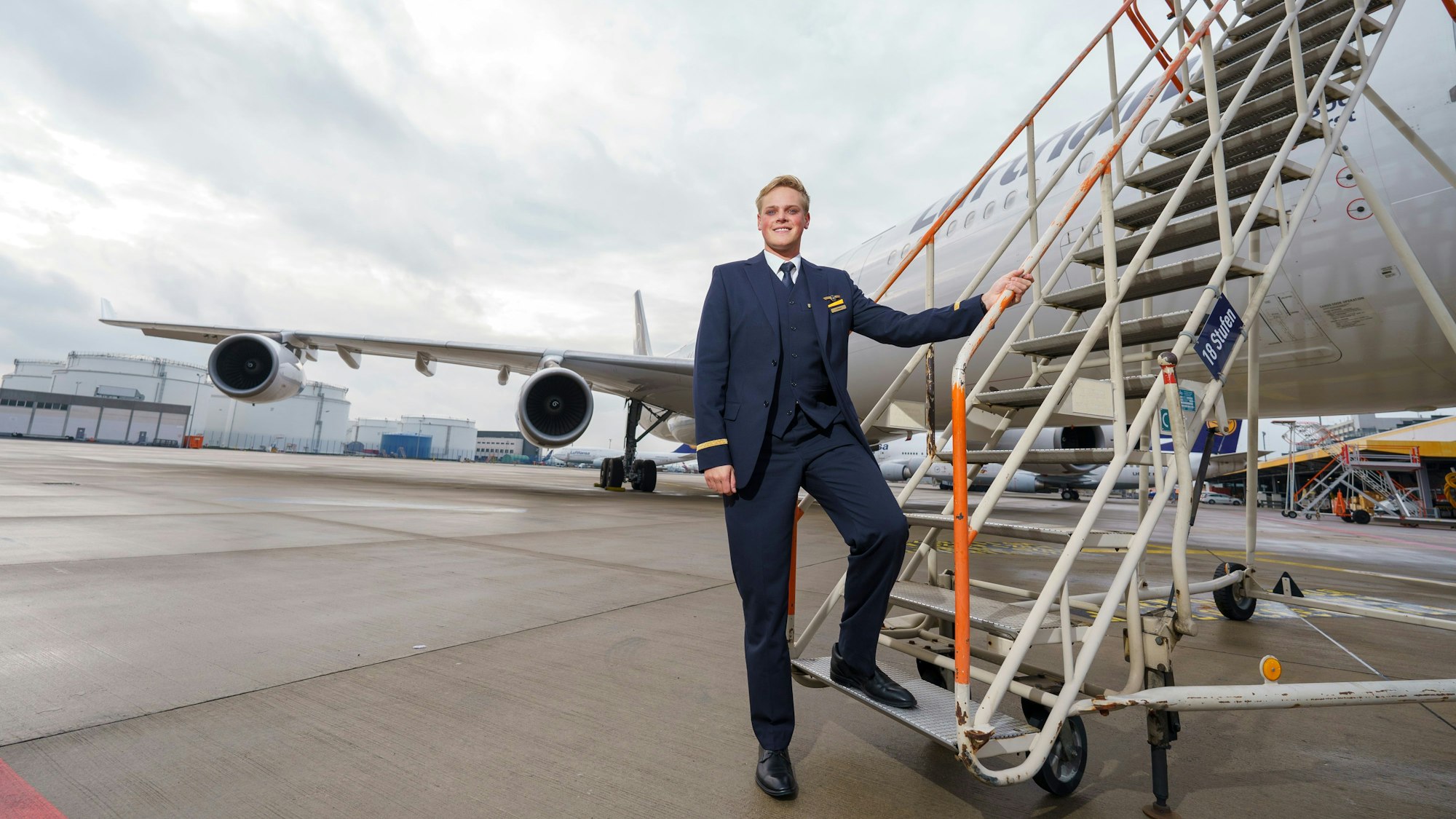 Alexander Böhmer, Lufthansa-Flugbegleiter, steht in Dienstuniform an einer Treppe zu einer Maschine seiner Fluggesellschaft.