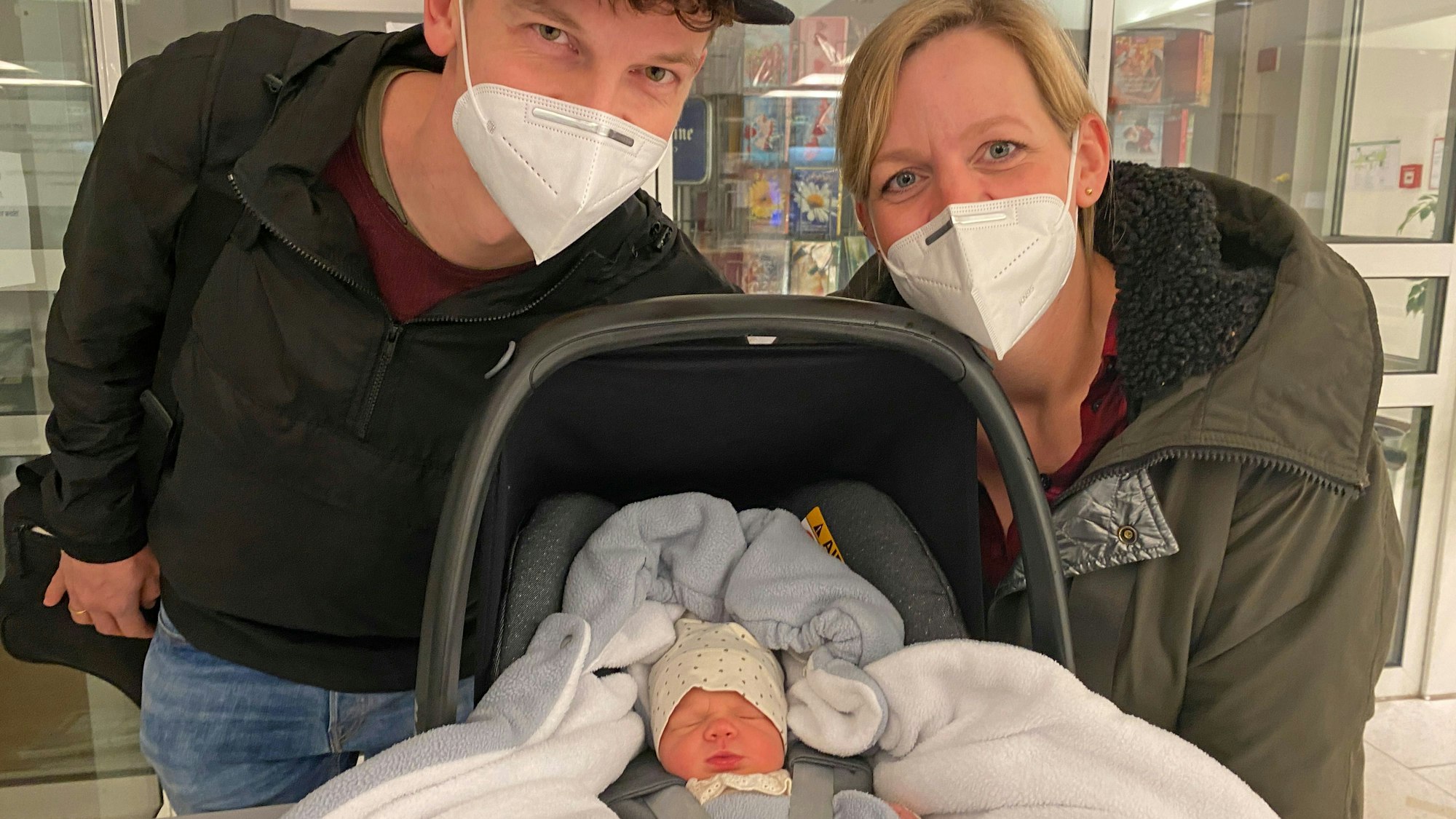 Ein Mann und eine Frau freuen sich über ihr neugeborenes Kind, das in einer Trage liegt.
