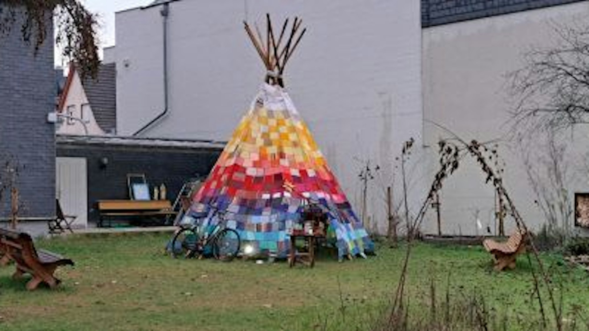 Ein buntes Tipi steht in einem Garten. An ihm lehnt ein Fahrrad.