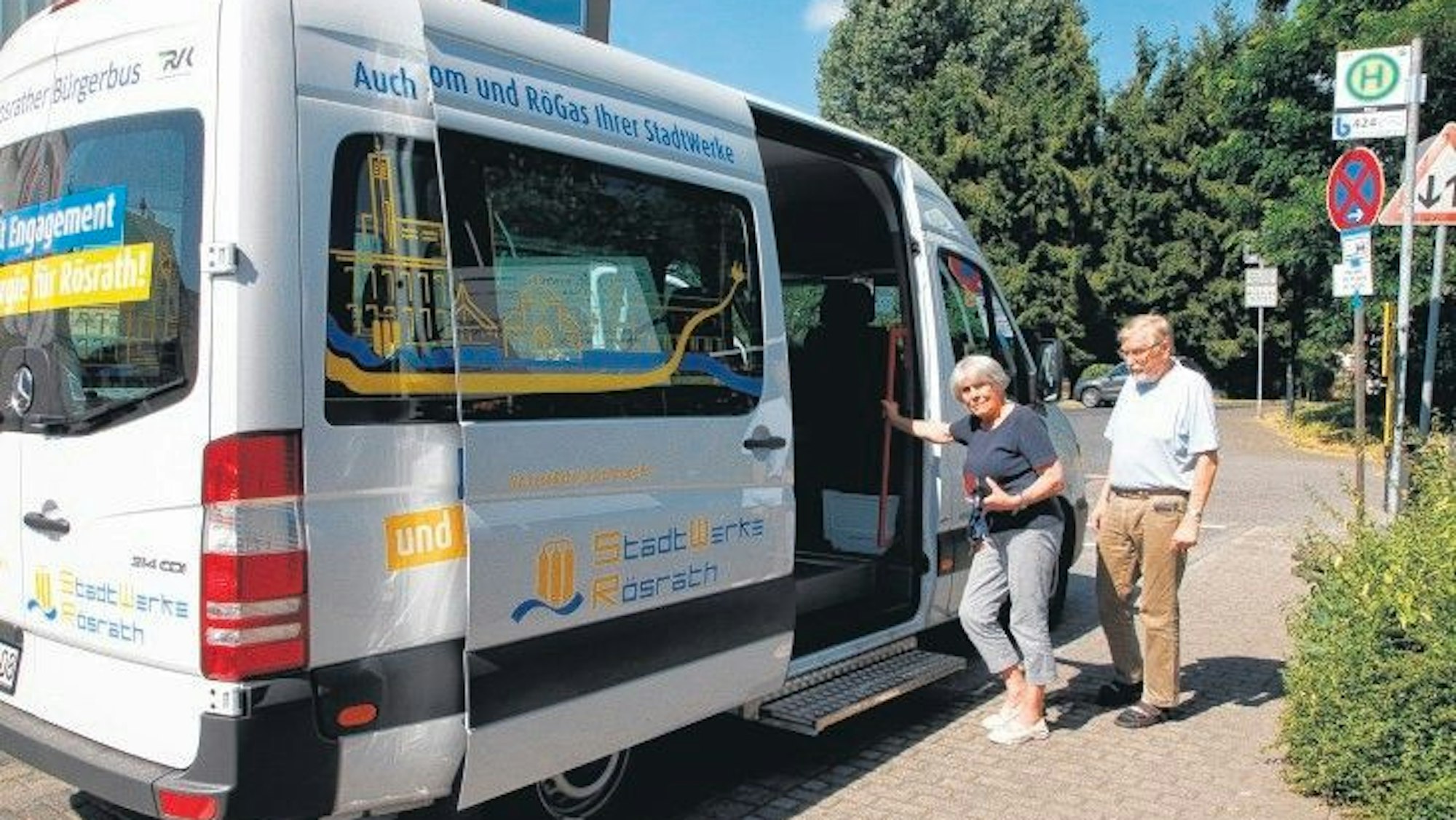 Eine Frau und ein Mann wollen an der Haltestelle Bitze in den Rö-Bus, den weißen Rösrather Bürgerbus, einsteigen.