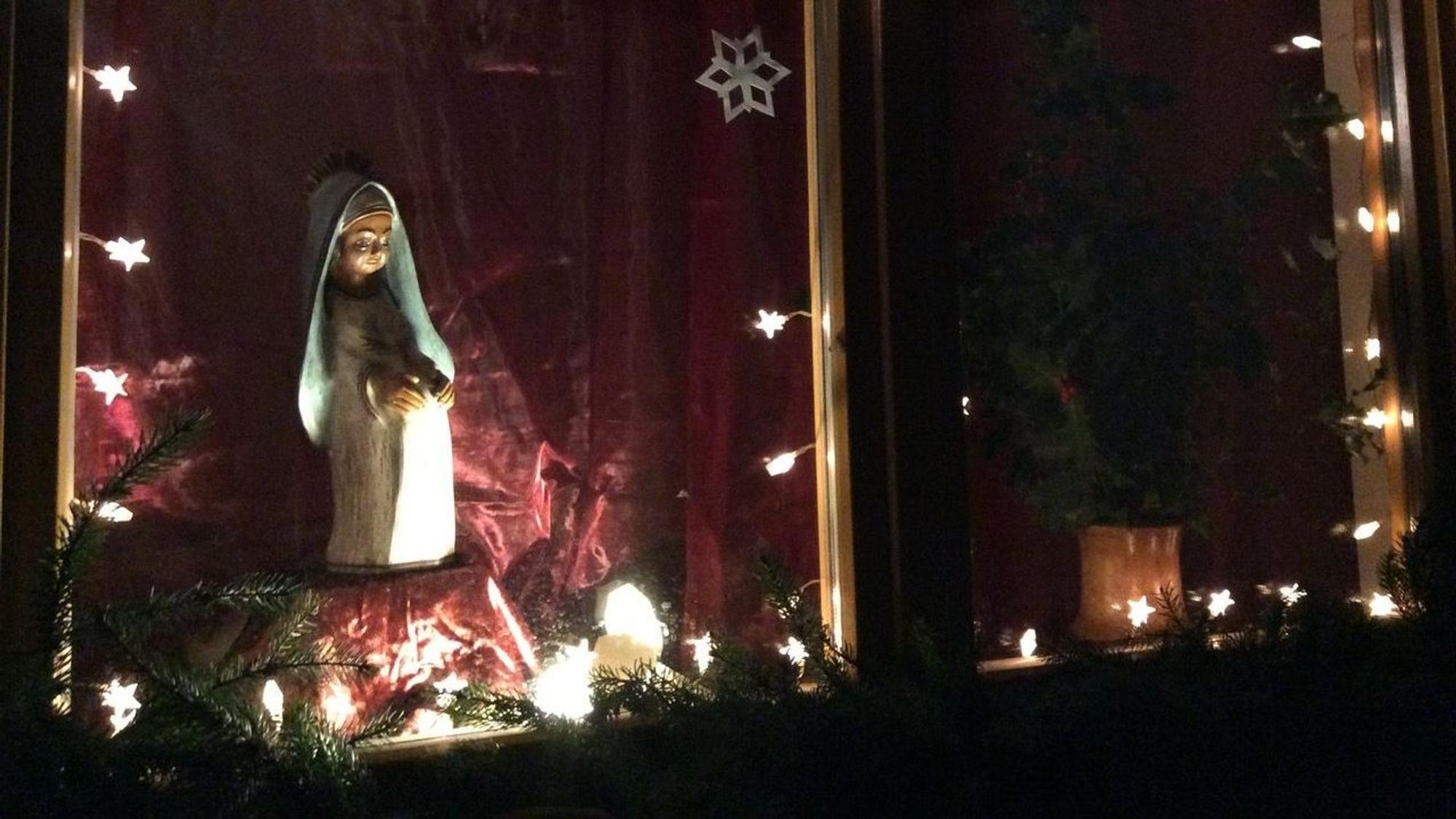 Eine schwangere Marienfigur wird vor rotem Hintergrund beleuchtet.