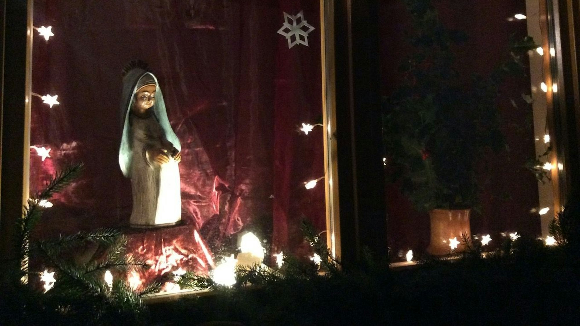 Eine schwangere Marienfigur wird vor rotem Hintergrund beleuchtet.