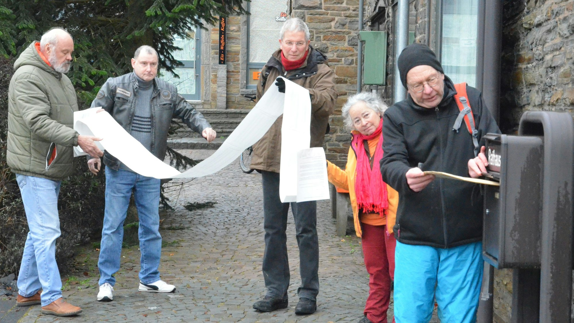 Ein Mann wirft die Petition in den Rathausbriefkasten, dahinter eine Frau und drei Männer mit einer sehr langen Liste.