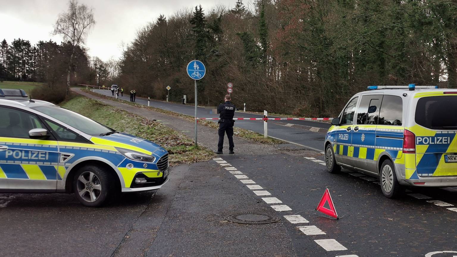 Zwei Streifenwagen stehen auf einer abgesperrten Straße, dazwischen ein Polizist.