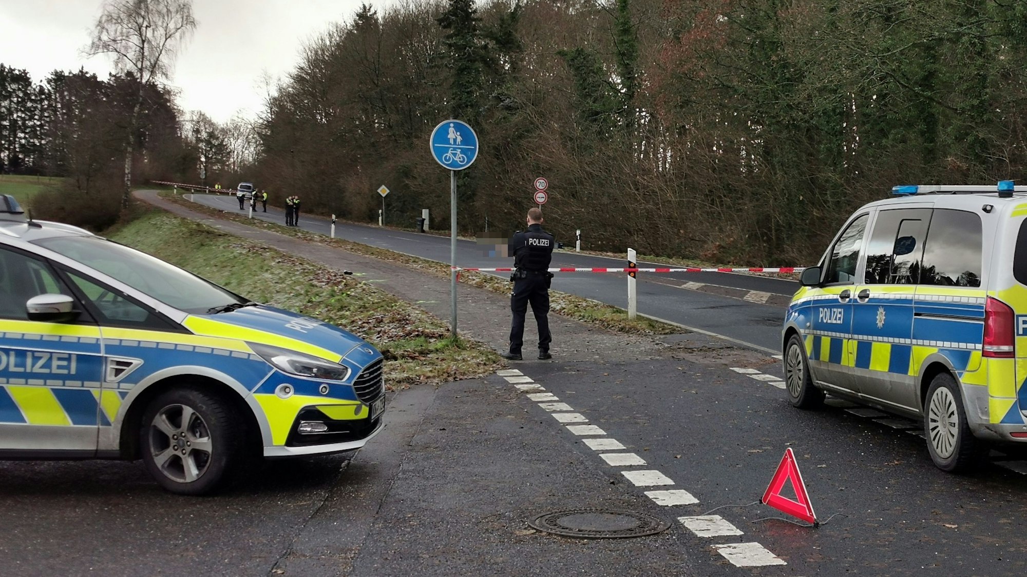 Zwei Streifenwagen stehen auf einer abgesperrten Straße, dazwischen ein Polizist.