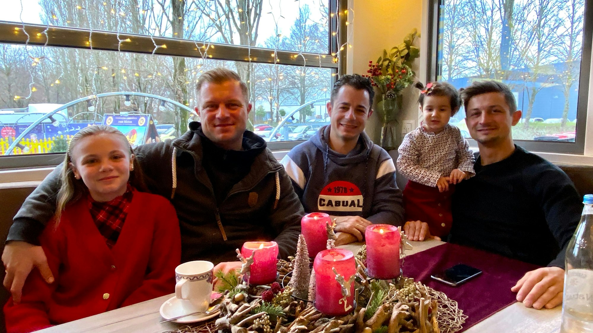 drei Männer und zwei Mädchen sitzen an einem weihnachtlich dekorierten Tisch vor einem Fenster