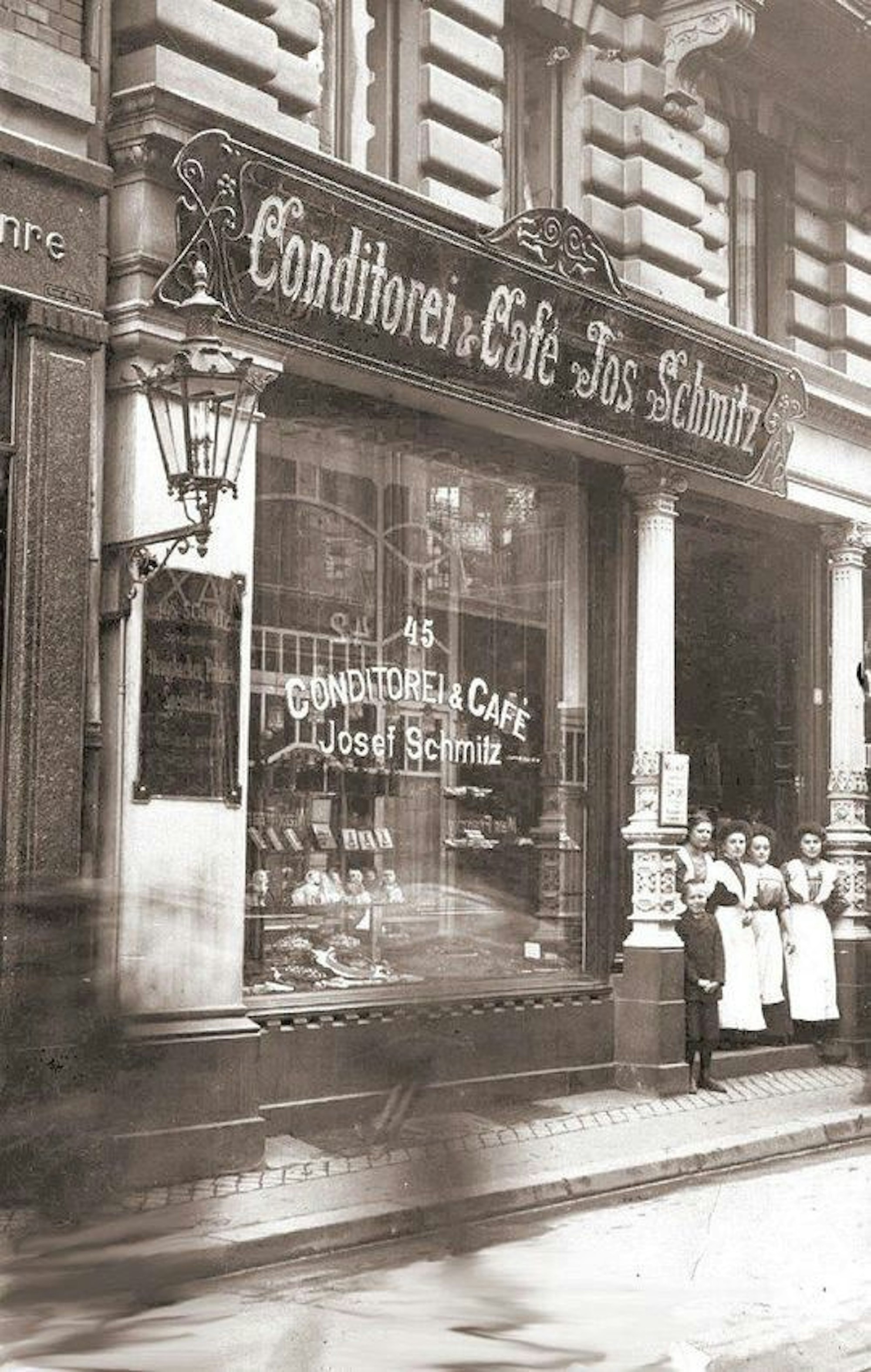 Historisches Foto vom ersten Geschäft an der Breite Straße, Frauen in langen weißen Schürzen und ein Junge stehen im Eingang.