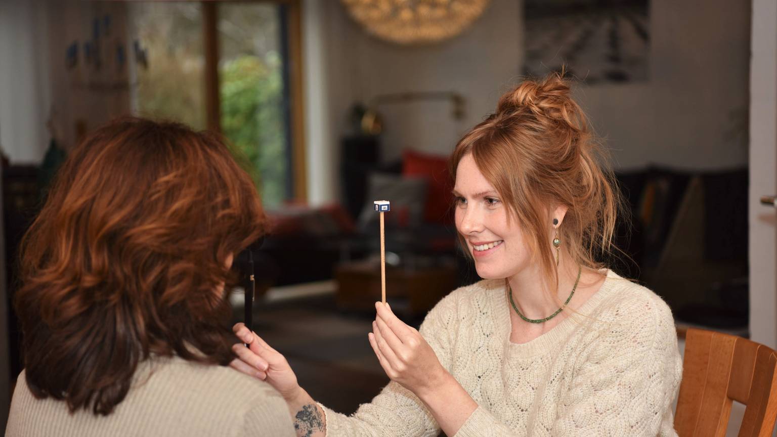 Orthoptistin Rebecca Decker sitzt vor einer Frau und hält ein Stäbchen zwischen ihre beiden Gesichter. Mit der anderen Hand hält sie eine Abdeckung vor ein Auge der Frau.