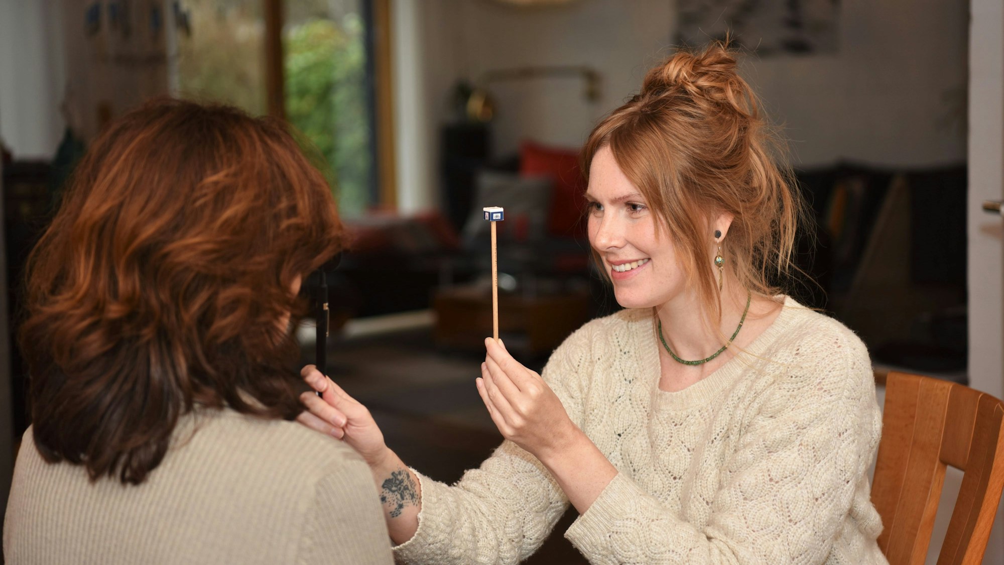 Orthoptistin Rebecca Decker sitzt vor einer Frau und hält ein Stäbchen zwischen ihre beiden Gesichter. Mit der anderen Hand hält sie eine Abdeckung vor ein Auge der Frau.