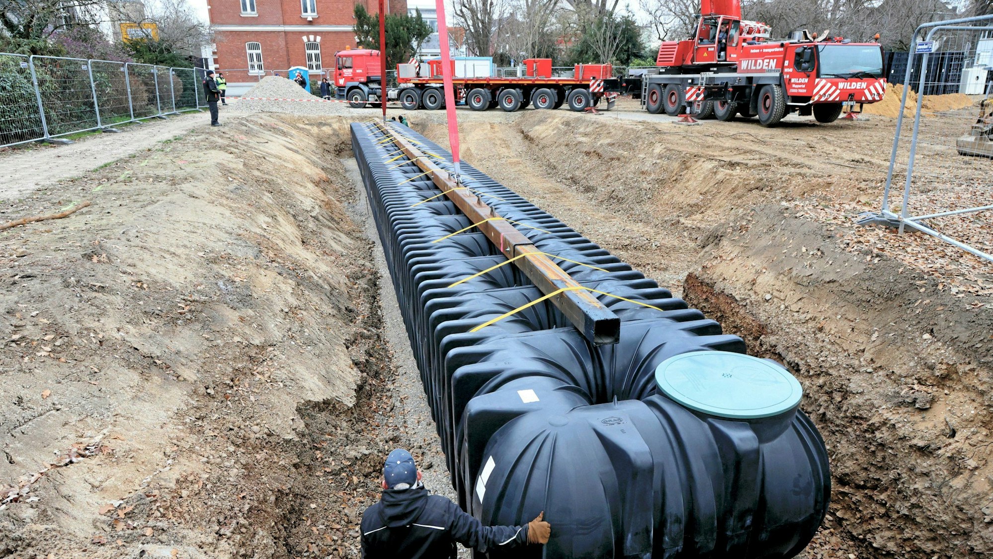 Die 30 Meter lange, schwarze Regenwasser-Zisterne aus Kunststoff wird von einem Autokran im alten Stadtpark abgesenkt.
