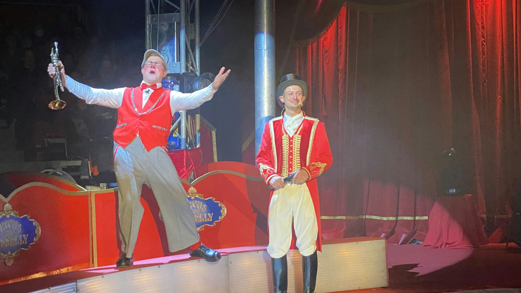 Ein Clown mit Trompete und ein Zirkusdirektor in einer Manege